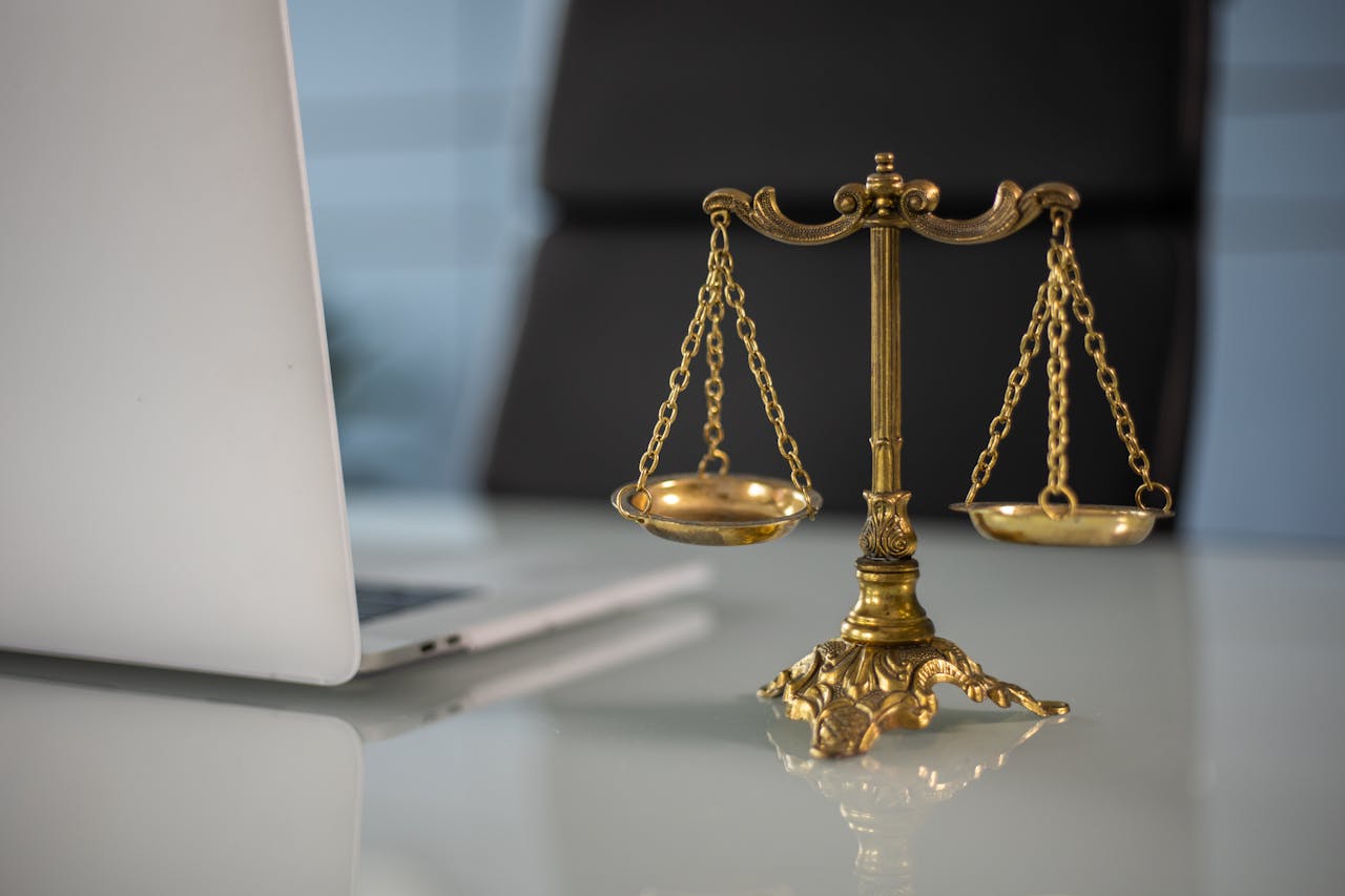 BEKIROGLU Law & Consultancy - International Law Firm .Golden justice scales on a desk beside a laptop, symbolizing law and balance.